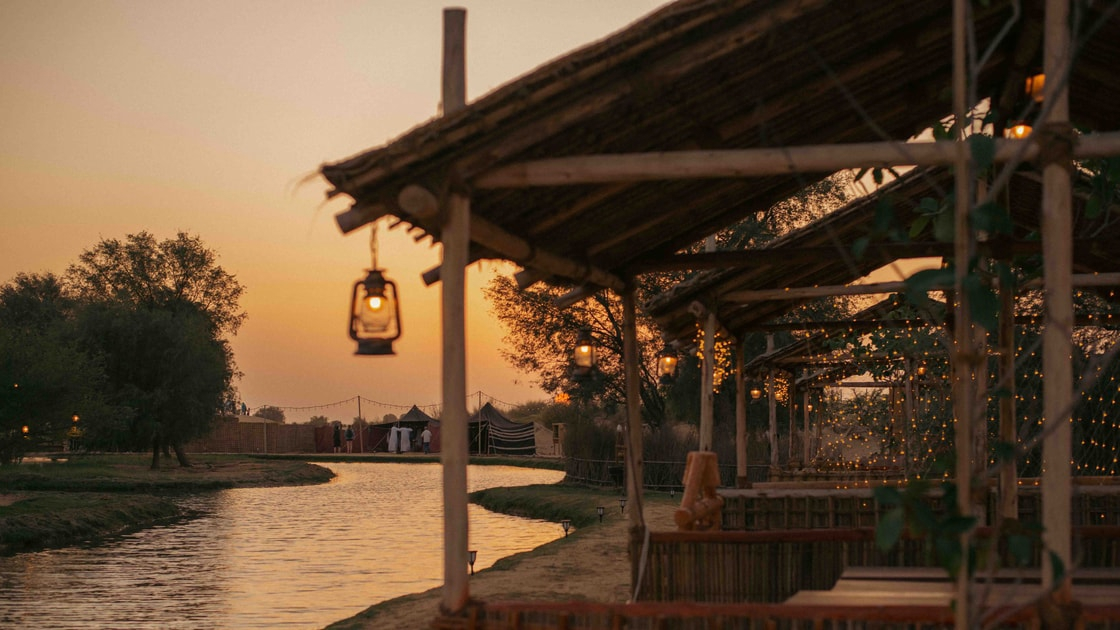 A lantern hanging in a palm-roofed shelter beside the oasis at Al Marmoom at sunset