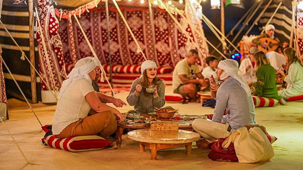 Guests sitting on cushions at low tables in a Bedouin tent for dinner