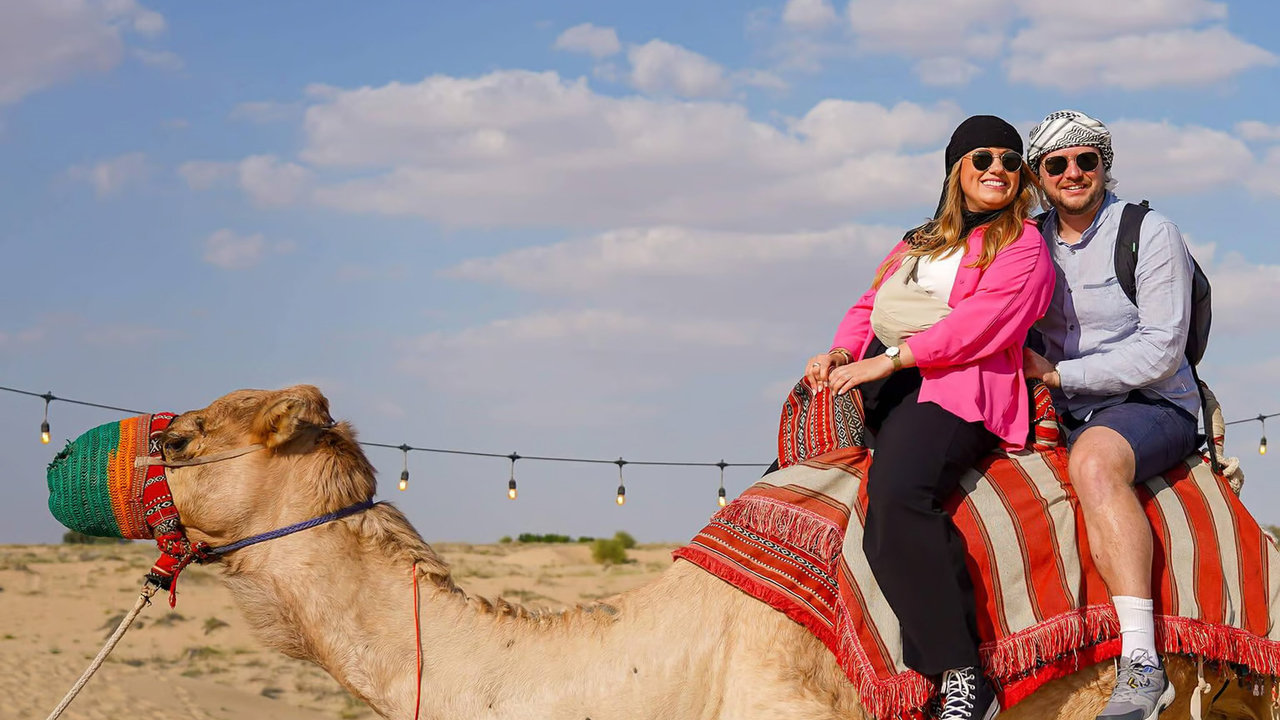 Two guests riding a camel across the sand at Al Marmoom